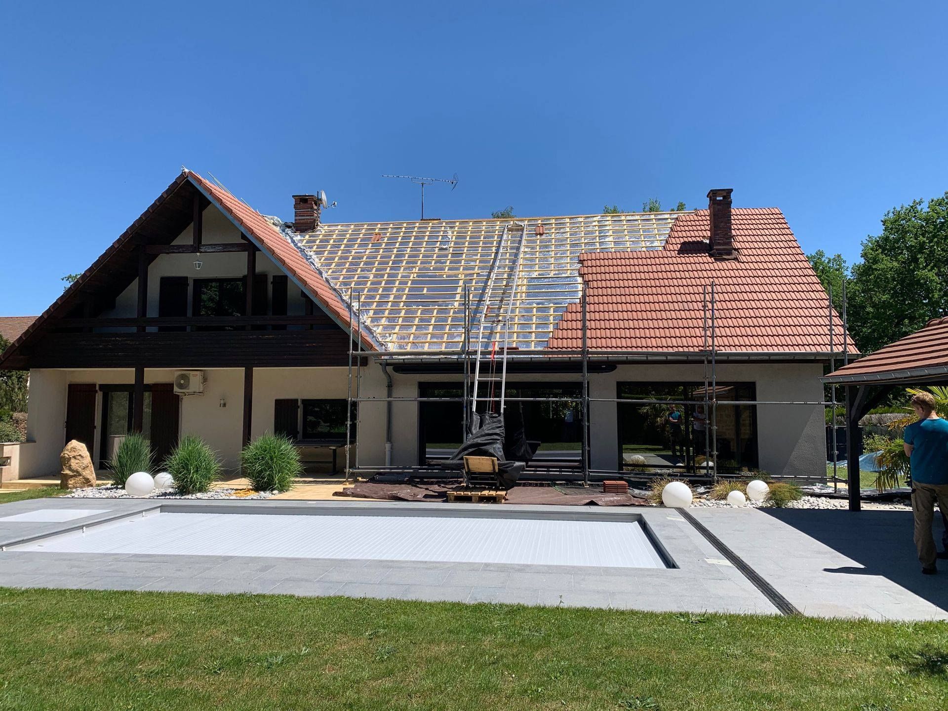 Maison avec toit en rénovation partielle et échafaudage, dans un jardin ensoleillé