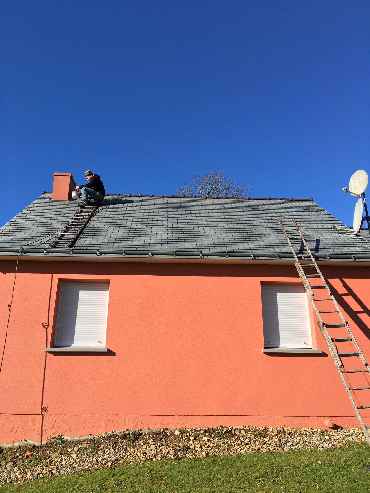 Artisan travaillant sur un toit en rénovation avec échelle posée sur la façade orange