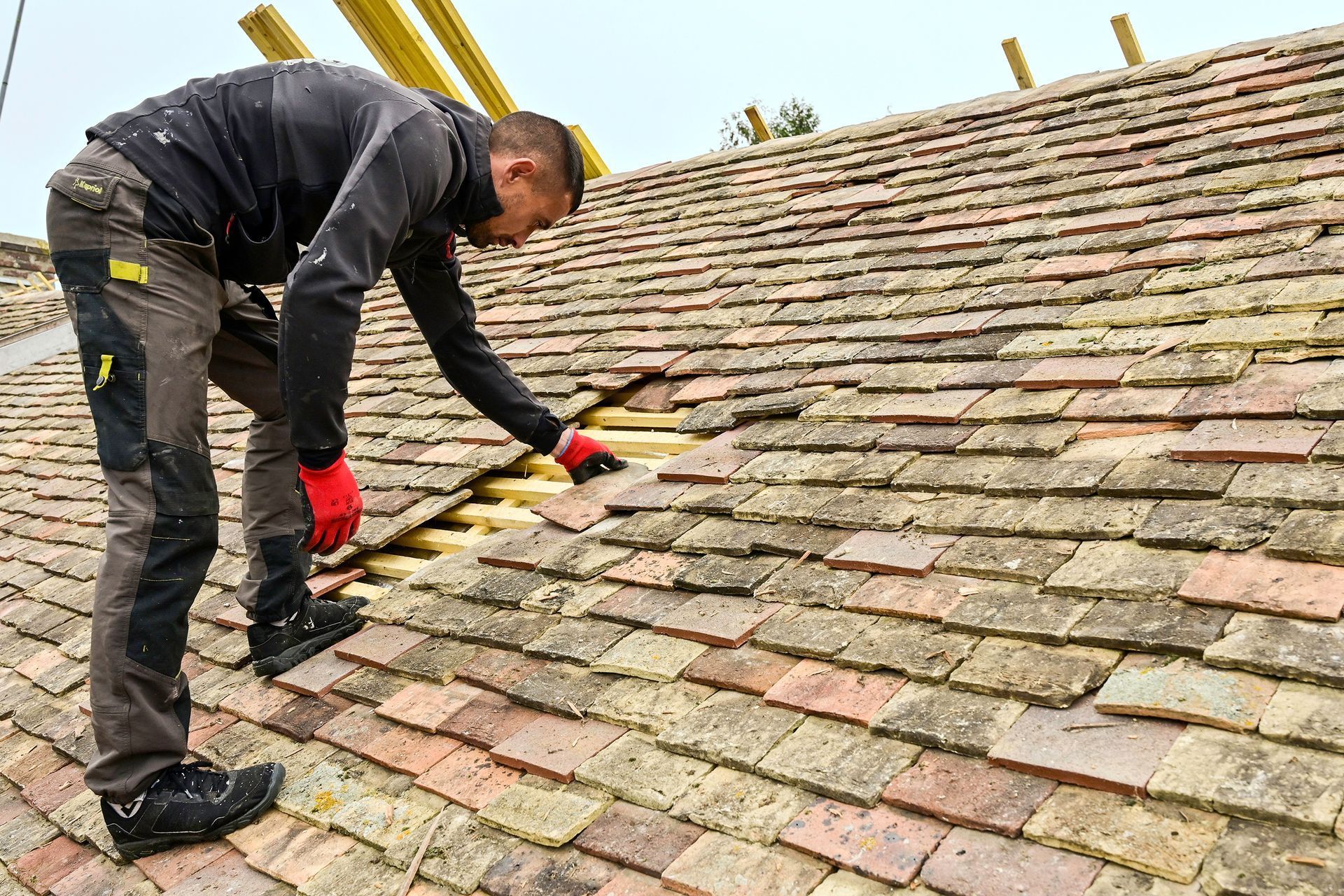 Artisan en train de réparer un toit en tuile avec des gants rouges
