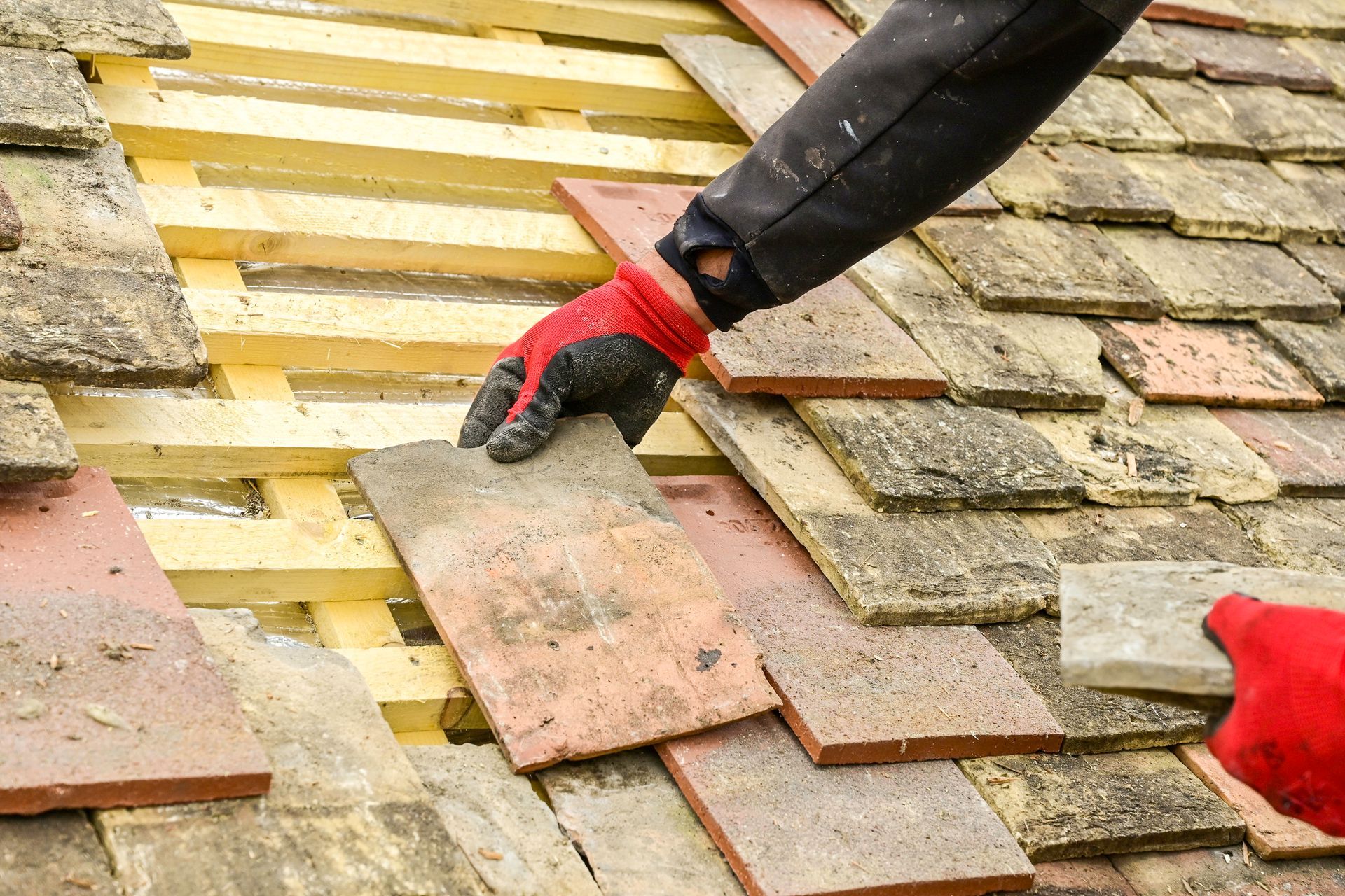 Main avec gant rouge posant une tuile sur une toiture en rénovation