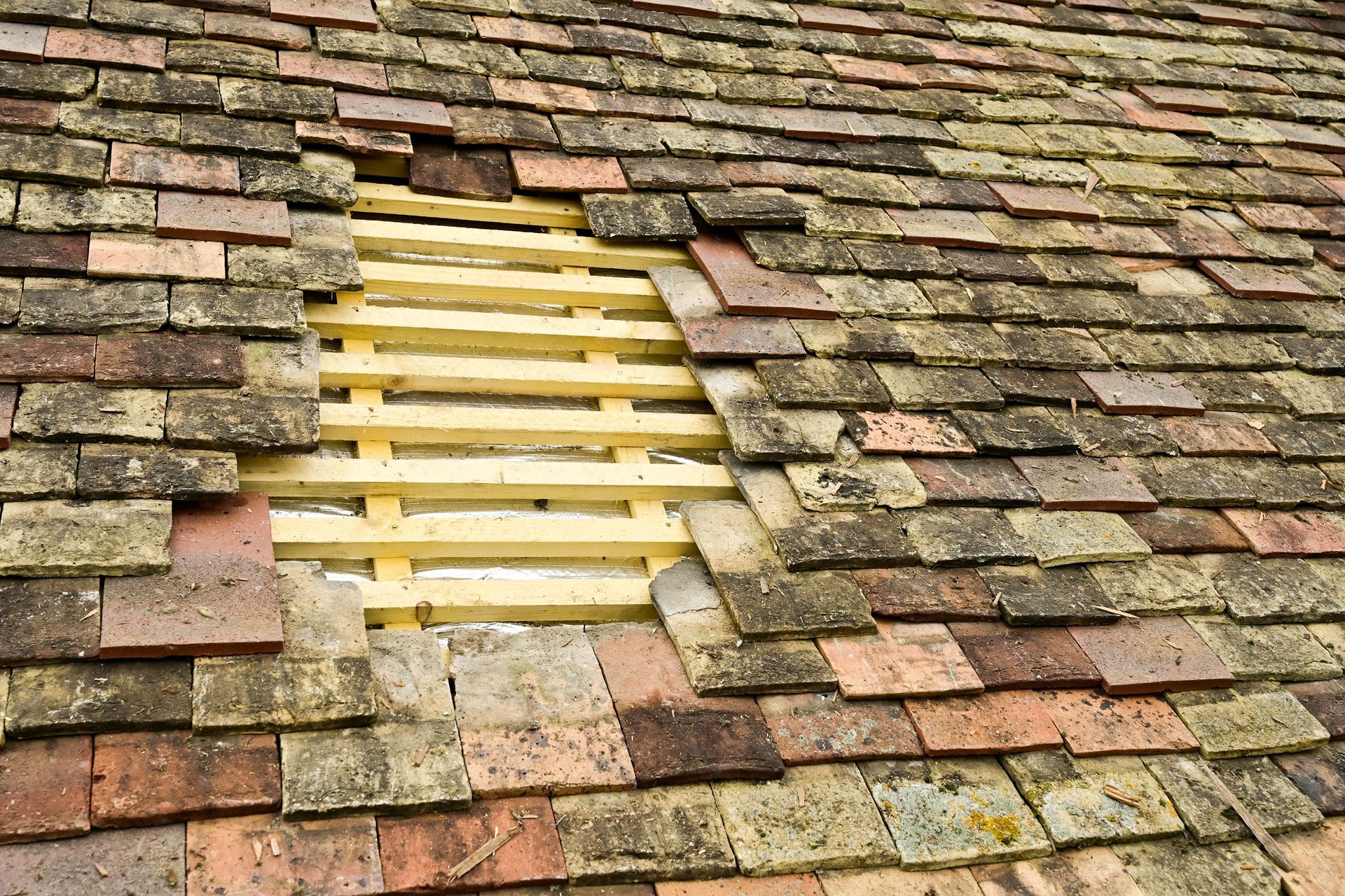 Toit en tuile ancienne avec une section ouverte laissant apparaître la charpente en bois