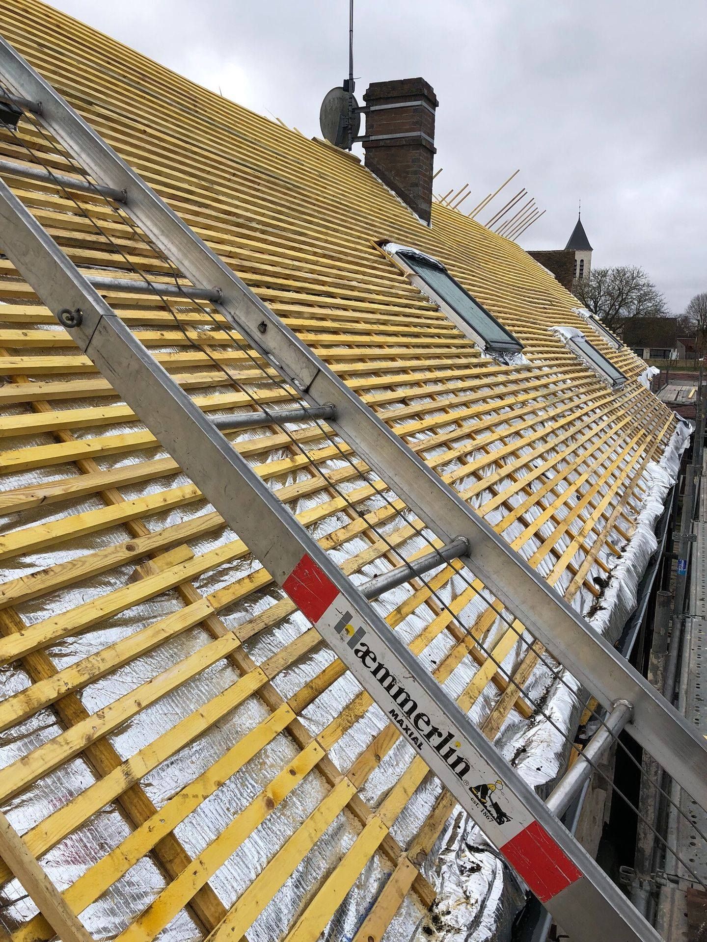 Échelle posée sur un toit en rénovation avec lattage en bois