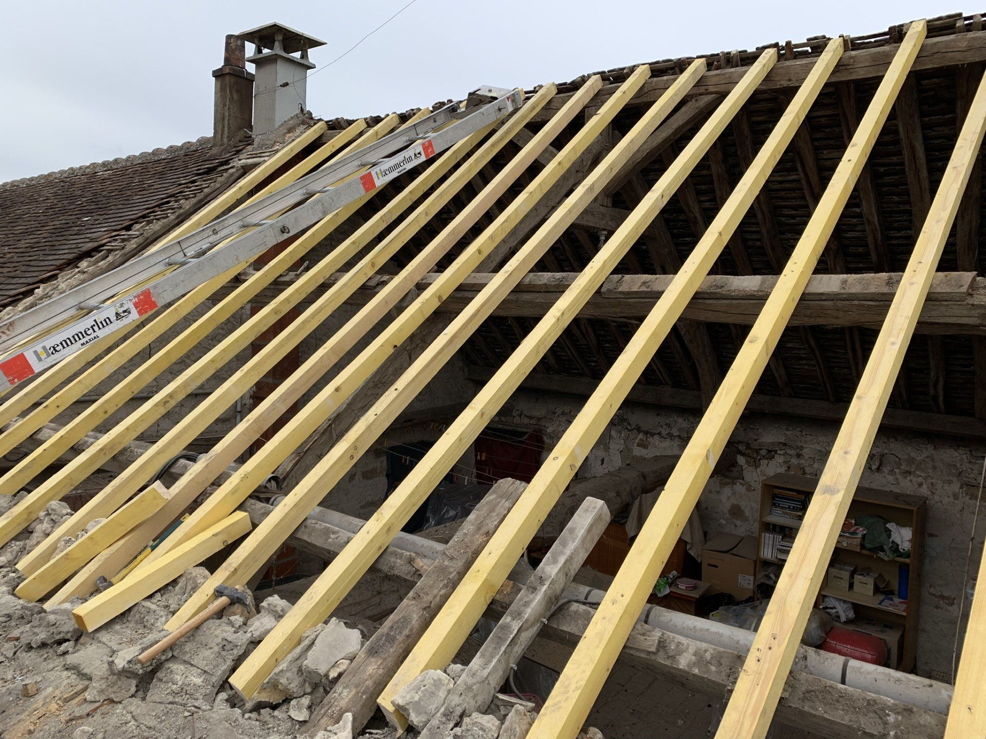 Toit en rénovation donnant sur l'intérieur de la maison avec lattage en bois visible et échelle posée sur la toiture 
