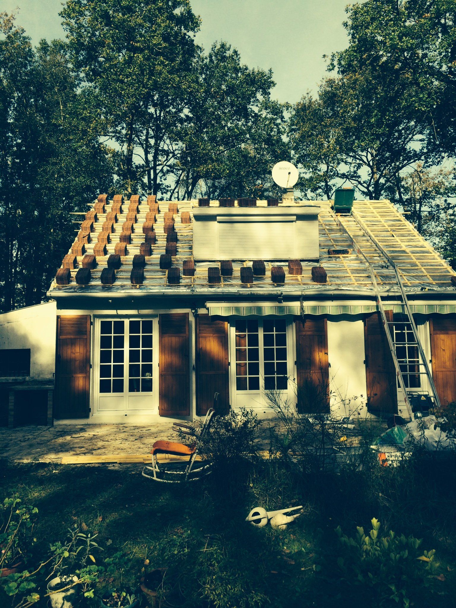 Maison en rénovation avec partie de la toiture retirée et échelle d'artisan posée contre la façade