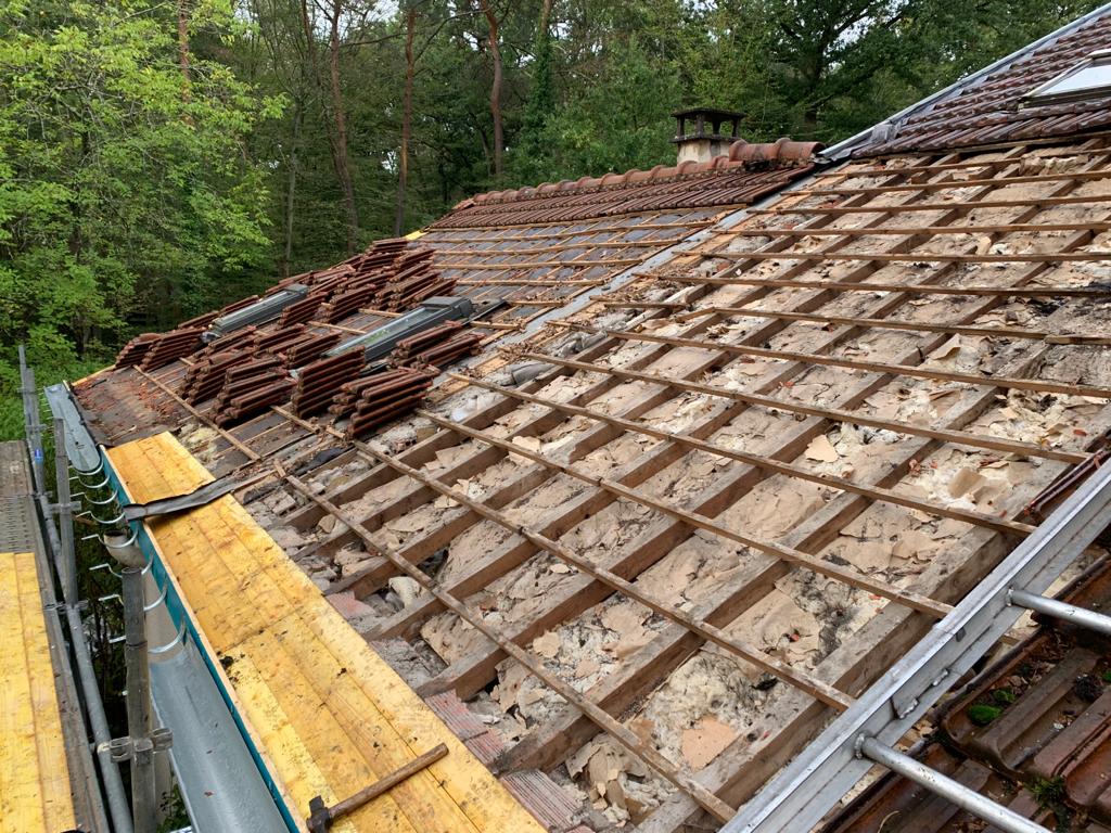 Toit en rénovation avec une partie de la couverture retirée et des piles de tuiles posées sur le côté