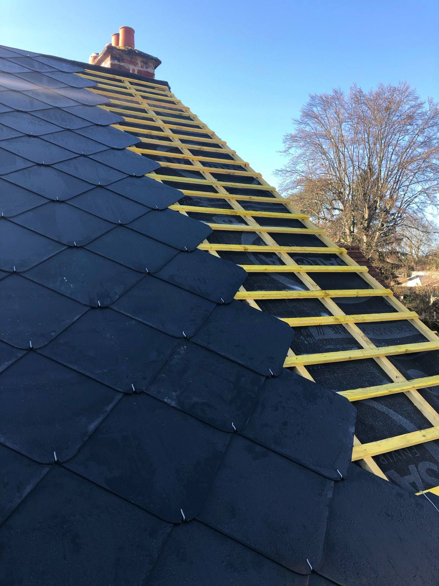 Toit en ardoise avec lattage jaune visible sur une partie de la surface droite