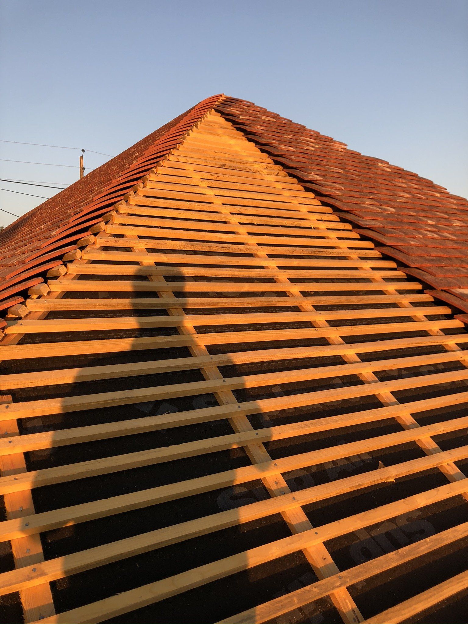 Toit en rénovation avec lattage en bois nouvellement installé et ombre d'un artisan visible