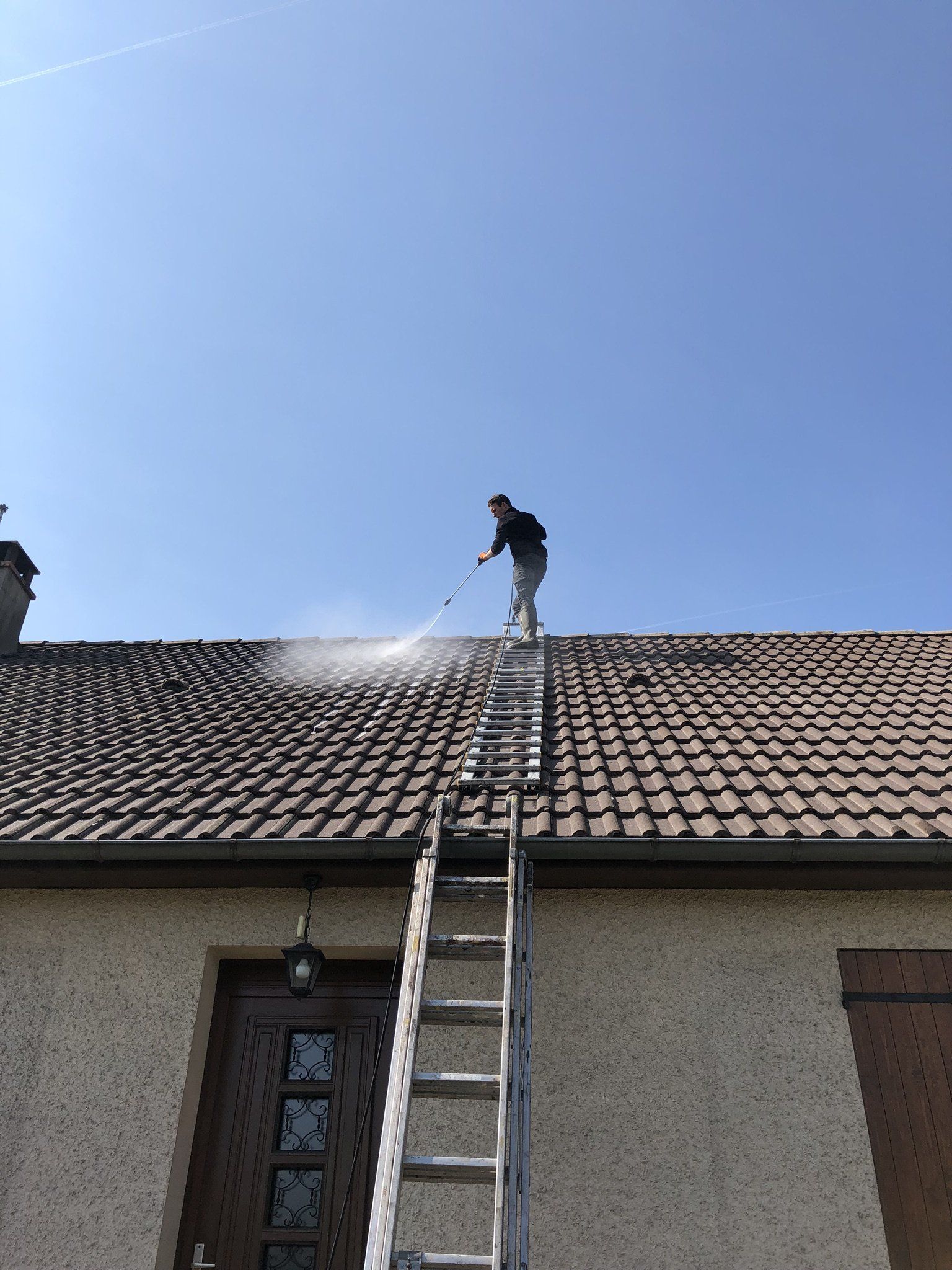 Artisan nettoyant un toit en tuile à l'aide d'un nettoyeur à haute pression