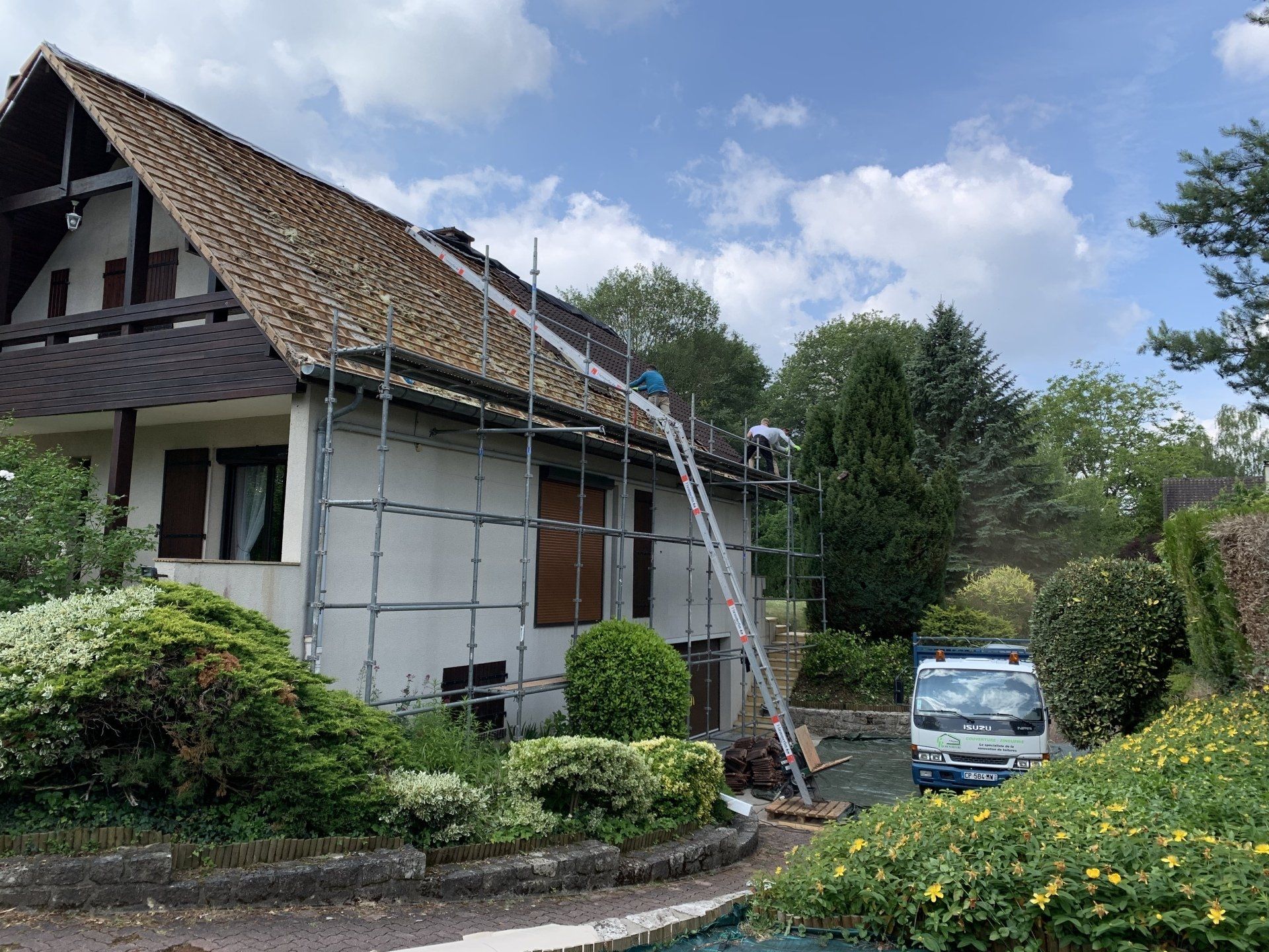 Maison ancienne à balcon avec toiture en tuile et échafaudage située dans un jardin arboré