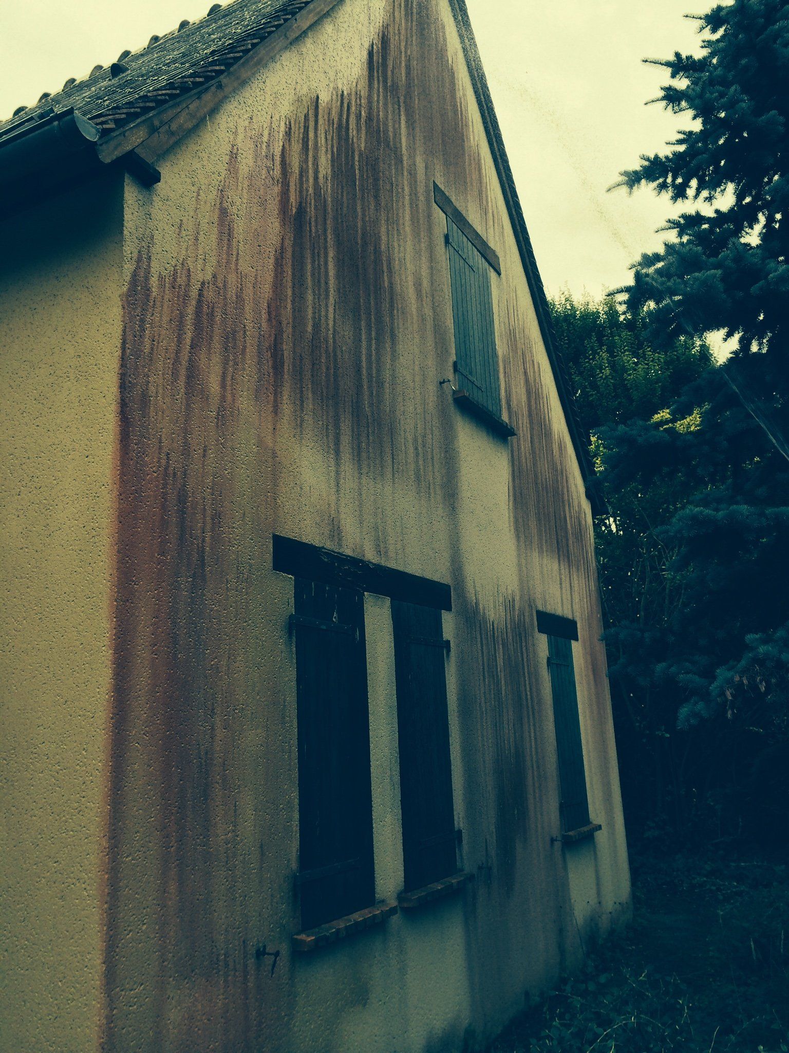 Maison ancienne avec façade en crépi usé et fenêtres à volets noirs