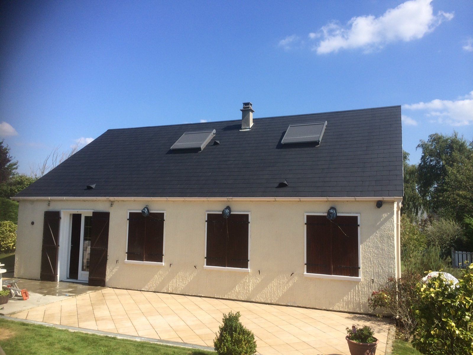 Maison avec toiture en ardoise noire et volets marron sur les fenêtres