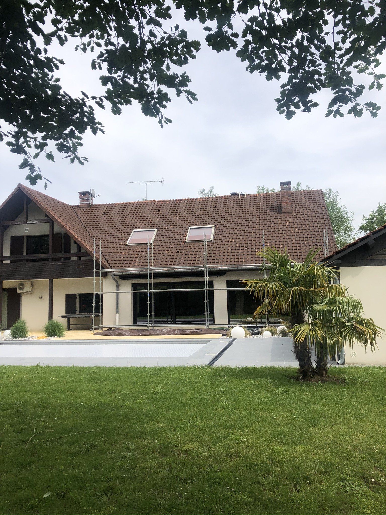 Maison avec toit en tuile rouge et véranda donnant sur un jardin et une piscine couverte
