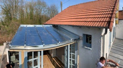 Maison avec toit en tuile rouge et véranda et artisan travaillant sur le côté