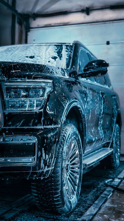 Un SUV noir est lavé dans une station de lavage automobile intérieure, recouvert de mousse de savon.
