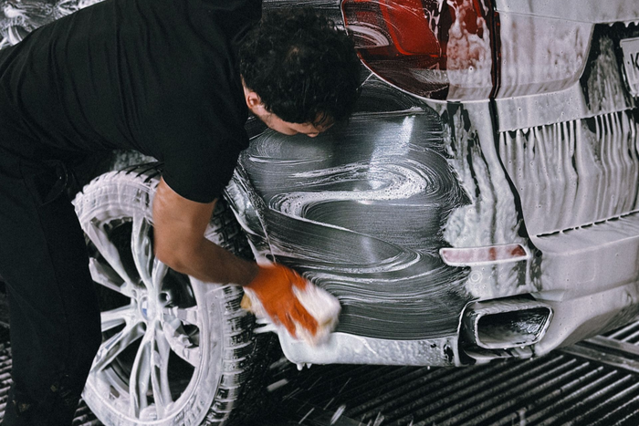 Une personne lave une voiture avec de la mousse savonneuse dans un centre de lavage auto.