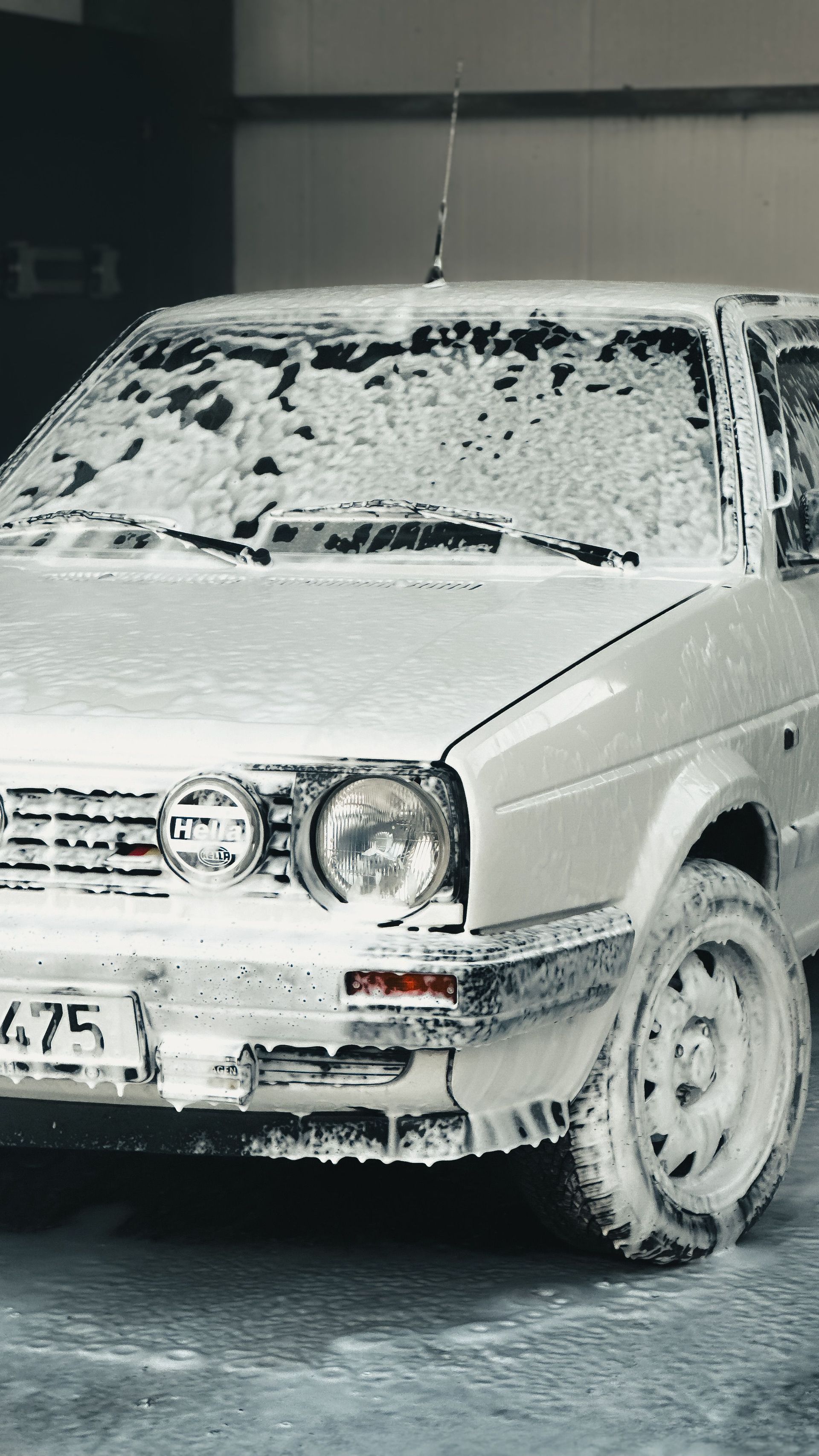 Berline blanche recouverte d'une épaisse couche de neige et de mousse, garée à l'extérieur en hiver
