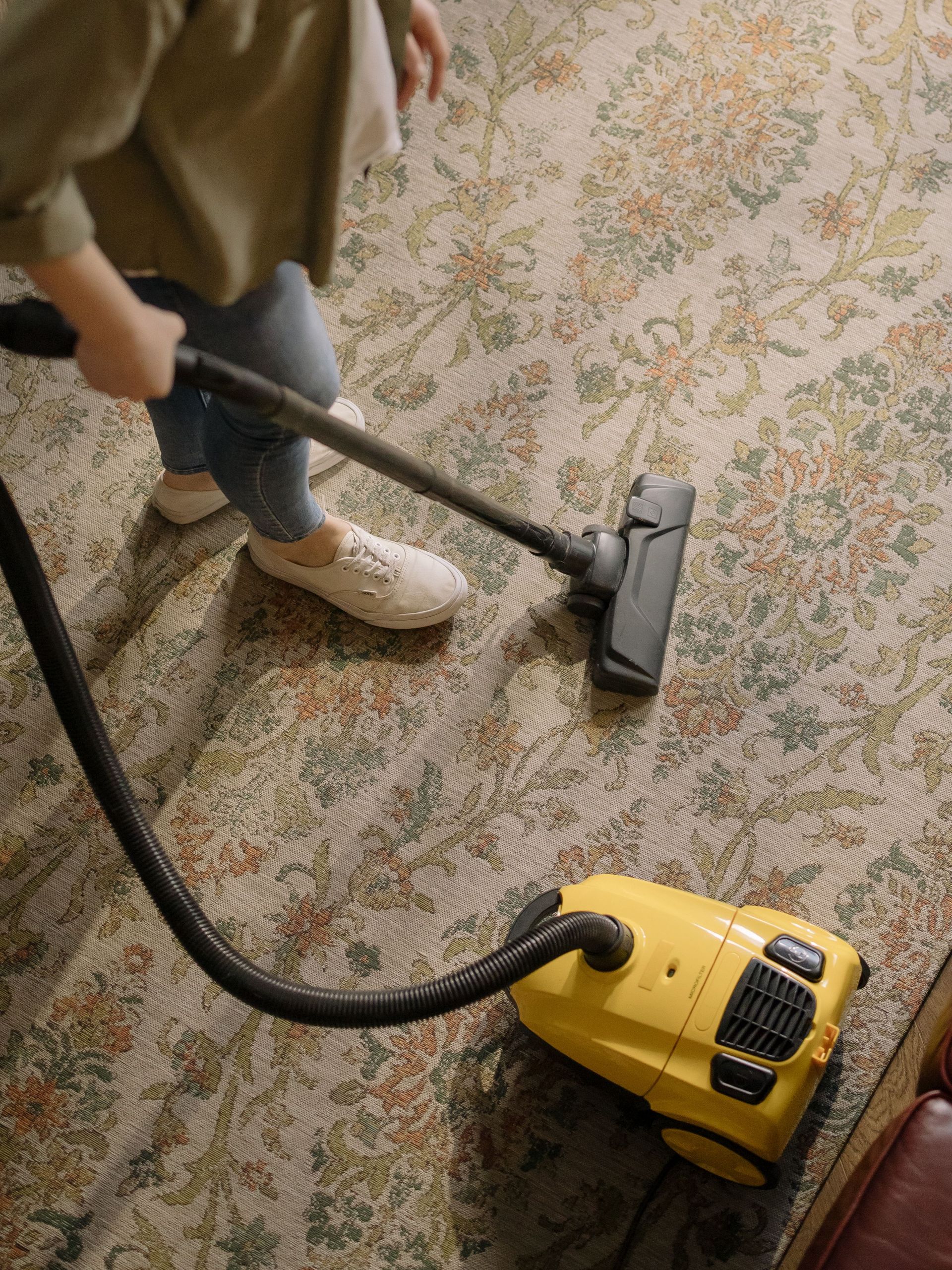 Une personne passe l'aspirateur sur un tapis à motifs floraux avec un aspirateur traîneau jaune.