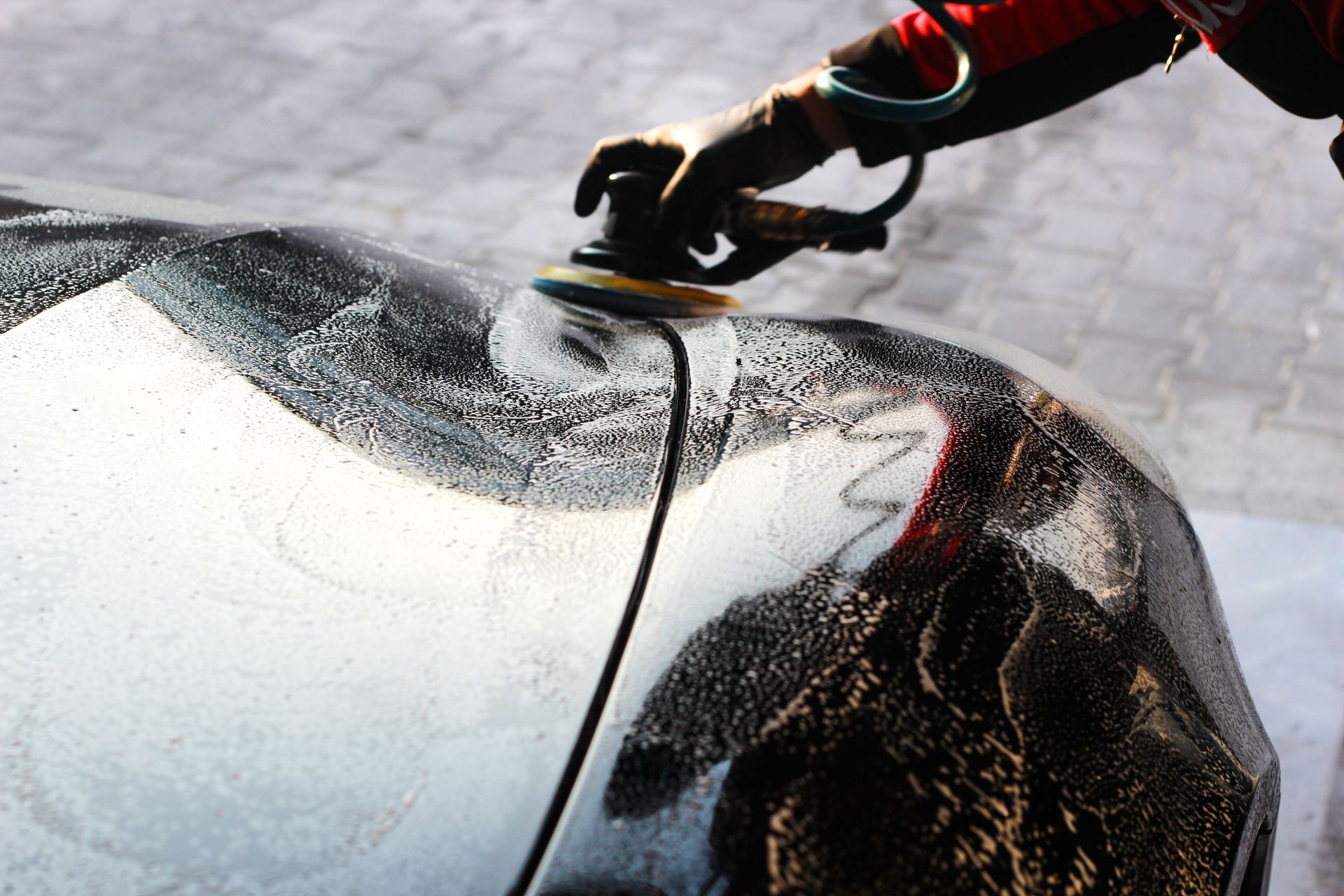 Une personne portant un gant noir utilise une lame de rasoir pour gratter la glace du pare-brise d'une voiture.