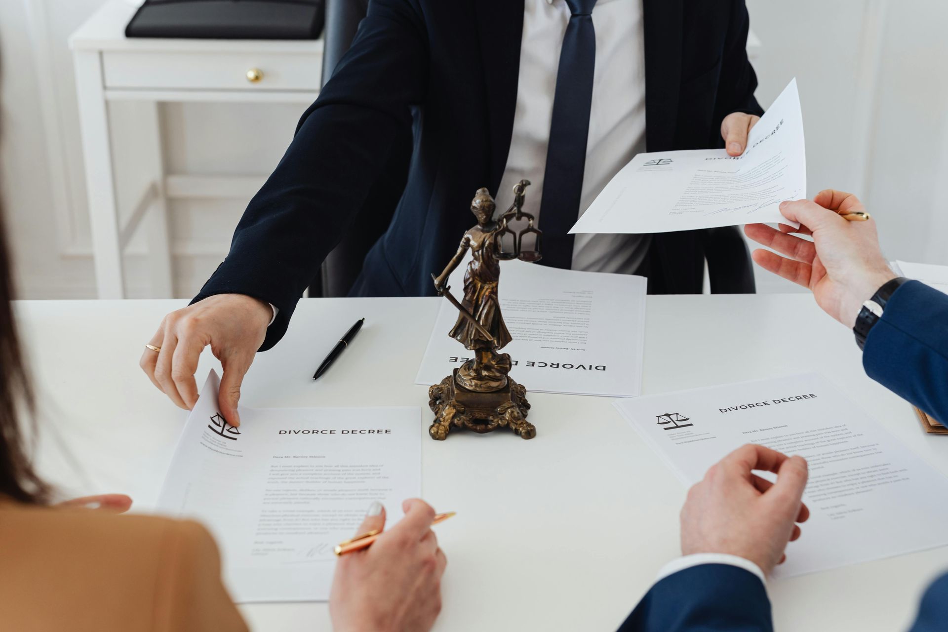 Un grupo de personas están sentadas en una mesa con papeles y una estatua de la justicia.
