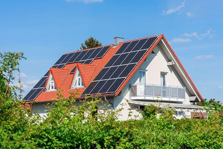 Ein Haus mit Solarzellen auf dem Dach ist von Bäumen umgeben.