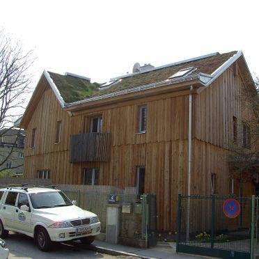 Vor einem Holzhaus parkt ein weißes Auto.