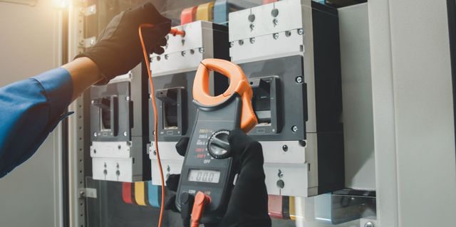 Elektriker testet mit einem Zangenamperemeter einen Sicherungskasten in einem Innenraum.