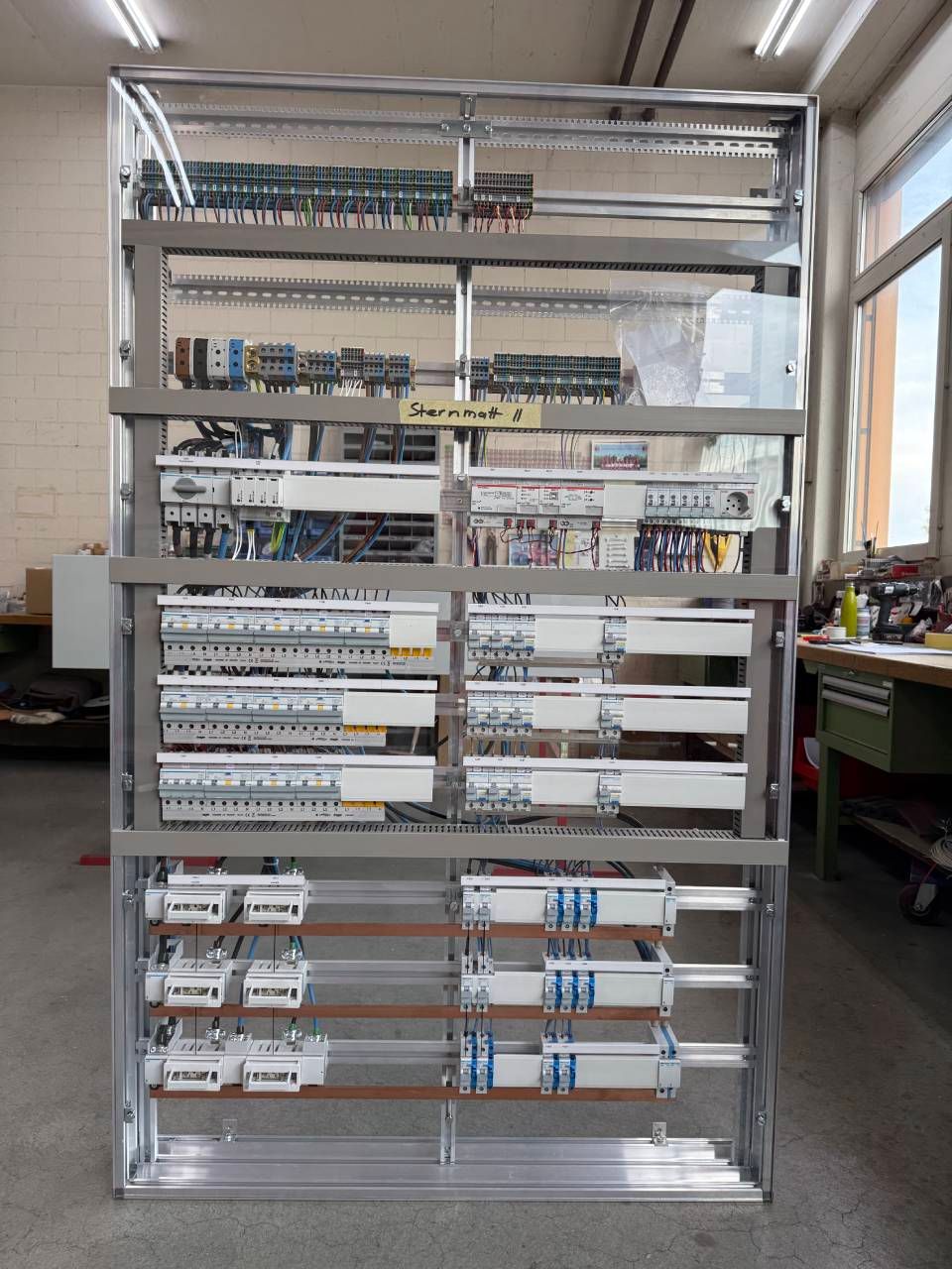 Wandmontierter elektrischer Schaltschrank mit Reihen von Leistungsschaltern, Relais und Verkabelung in einem Metallgehäuse