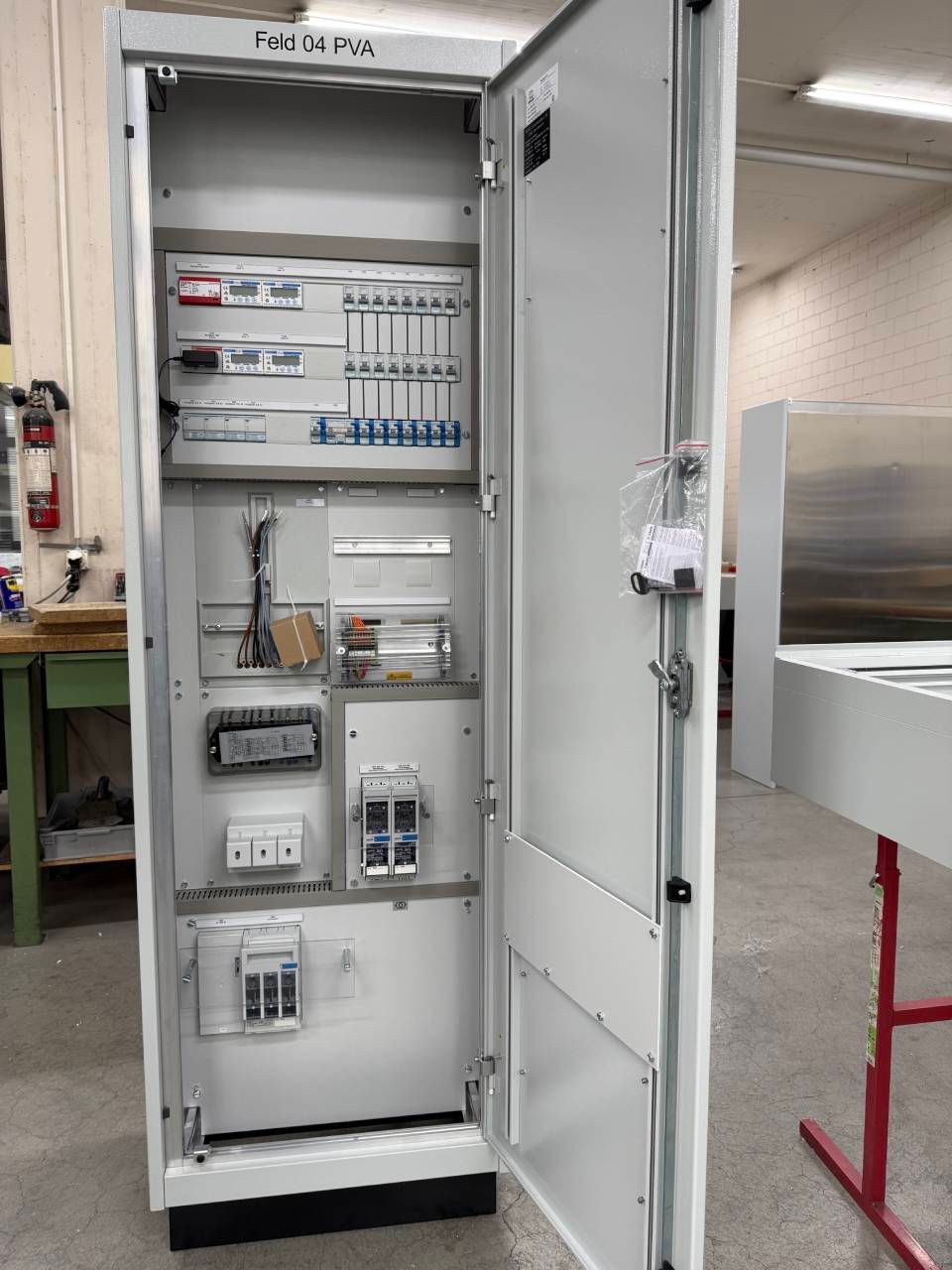 Offener elektrischer Schaltschrank mit Verkabelung, Schaltern und Schaltungskomponenten in einer Werkstatt.