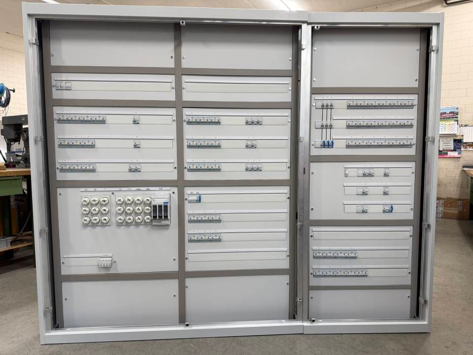 Offener elektrischer Schaltschrank mit Reihen von Sicherungsautomaten und Anschlussklemmen in einem grauen Metallgehäuse