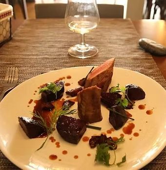 Assiette d'entrée gastronomique composée de légumes et d'herbes poêlés, présentée sur une table de restaurant, avec un verre de vin en arrière-plan.