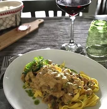 Des pâtes à la sauce crémeuse et aux herbes, servies dans une assiette blanche, sur une table à manger avec du vin et des verres.