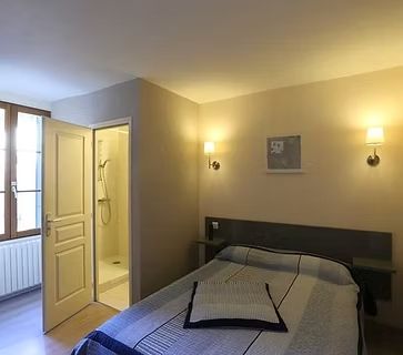 Chambre confortable avec lit double, appliques murales, porte de salle de bains ouverte et fenêtre avec radiateur.