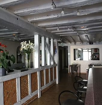 Intérieur de café moderne avec poutres blanches, plantes et sièges de bar le long d'un comptoir rustique.