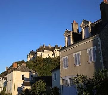 Maisons ensoleillées à flanc de colline, avec un château sur la colline sous un ciel bleu limpide.