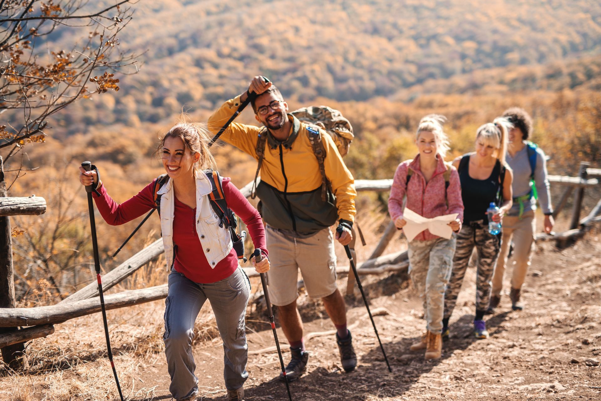 Des randonneurs gravissent un sentier aride à flanc de colline, s'appuyant sur des bâtons de marche sous un soleil chaud.