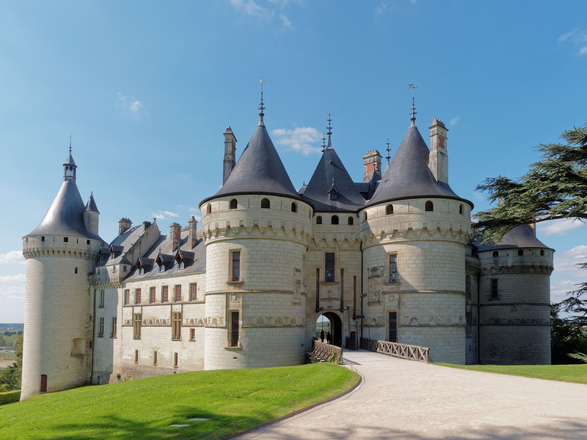 Château de pierre aux tours coniques au bord d'un chemin herbeux sous un ciel bleu limpide.