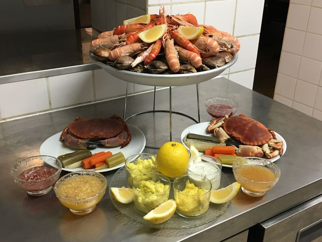 Plateau de fruits de mer sur un comptoir, avec pattes de crabe, palourdes, quartiers de citron et sauces.