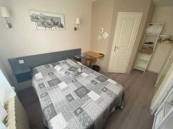 Petite chambre avec un lit, un bureau, des étagères ouvertes et une décoration grise dans un coin bien rangé.