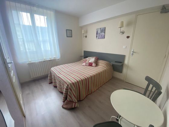 Petite chambre avec un lit simple, une fenêtre avec des voilages, une table ronde et une chaise.