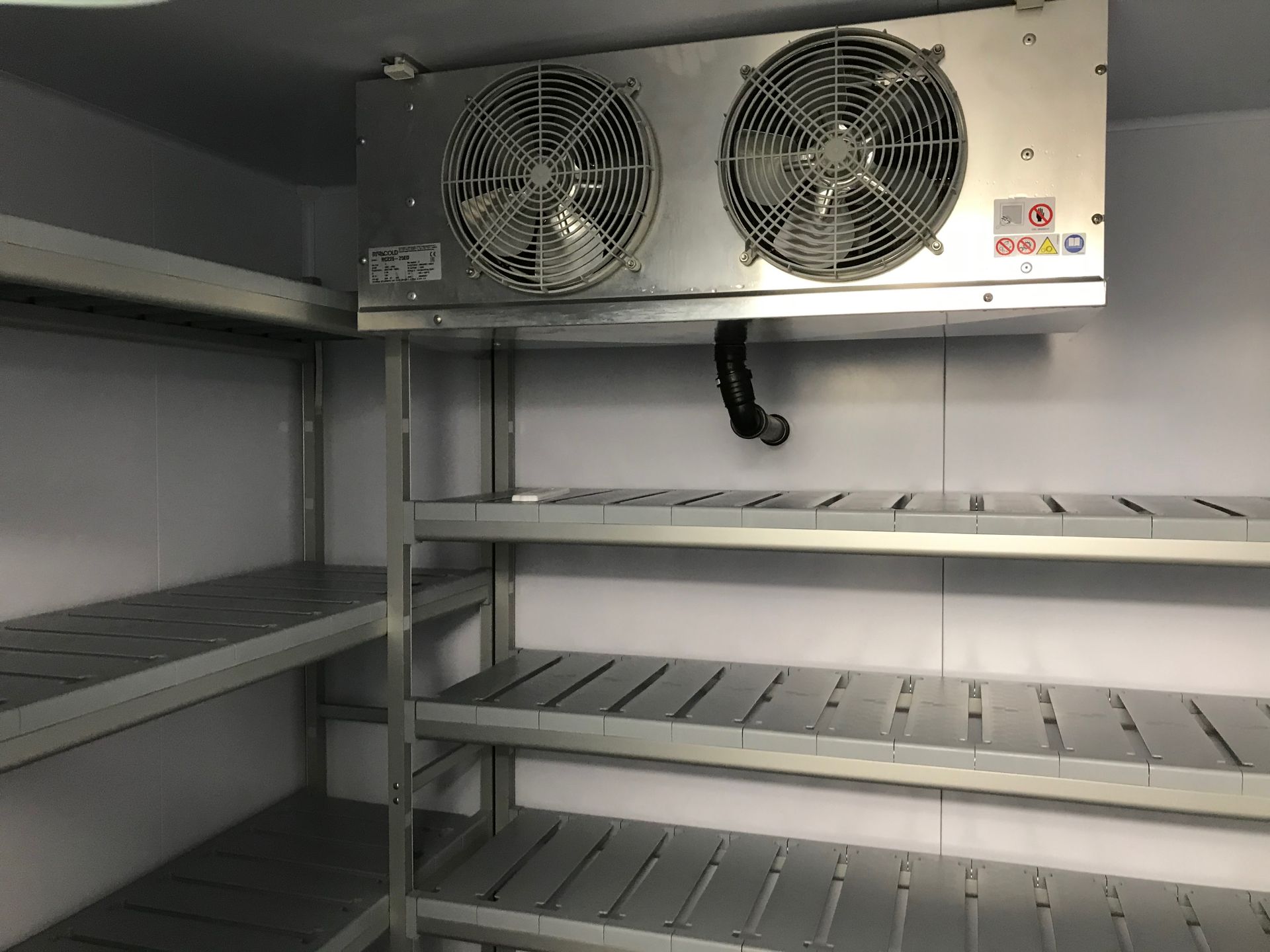 Interno di una cella frigorifera, con ripiani e un'unità di raffreddamento a doppia ventola montata sul soffitto.