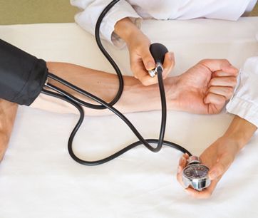 Medición de la presión arterial en el brazo de un paciente con un manguito y un estetoscopio en una cama.