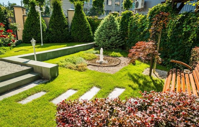Sonniger, angelegter Garten mit Steinstufen, Brunnen, geschnittenen Hecken und einer Holzbank