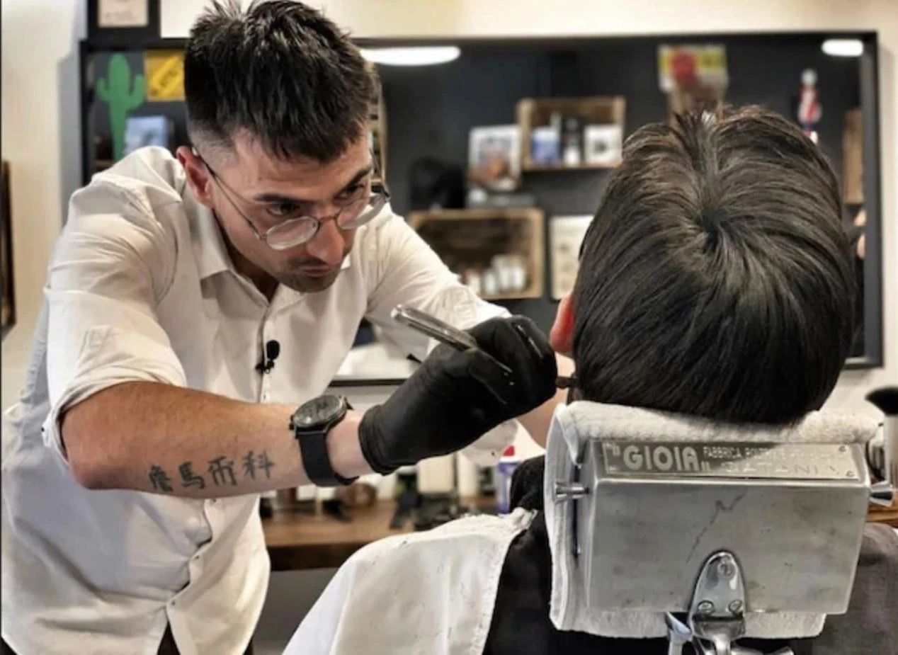 Un barbiere usa il tagliacapelli per tagliare i capelli di un uomo, profilo laterale, in un interno.