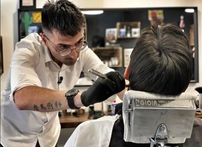 Un barbiere usa il tagliacapelli per tagliare i capelli di un uomo, profilo laterale, in un interno.