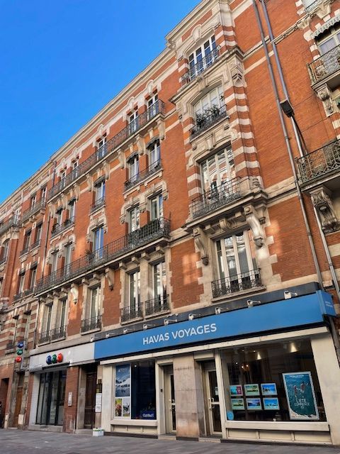 Immeuble parisien en briques rouges orné, avec une façade bleue « Havas Voyages » au rez-de-chaussée.