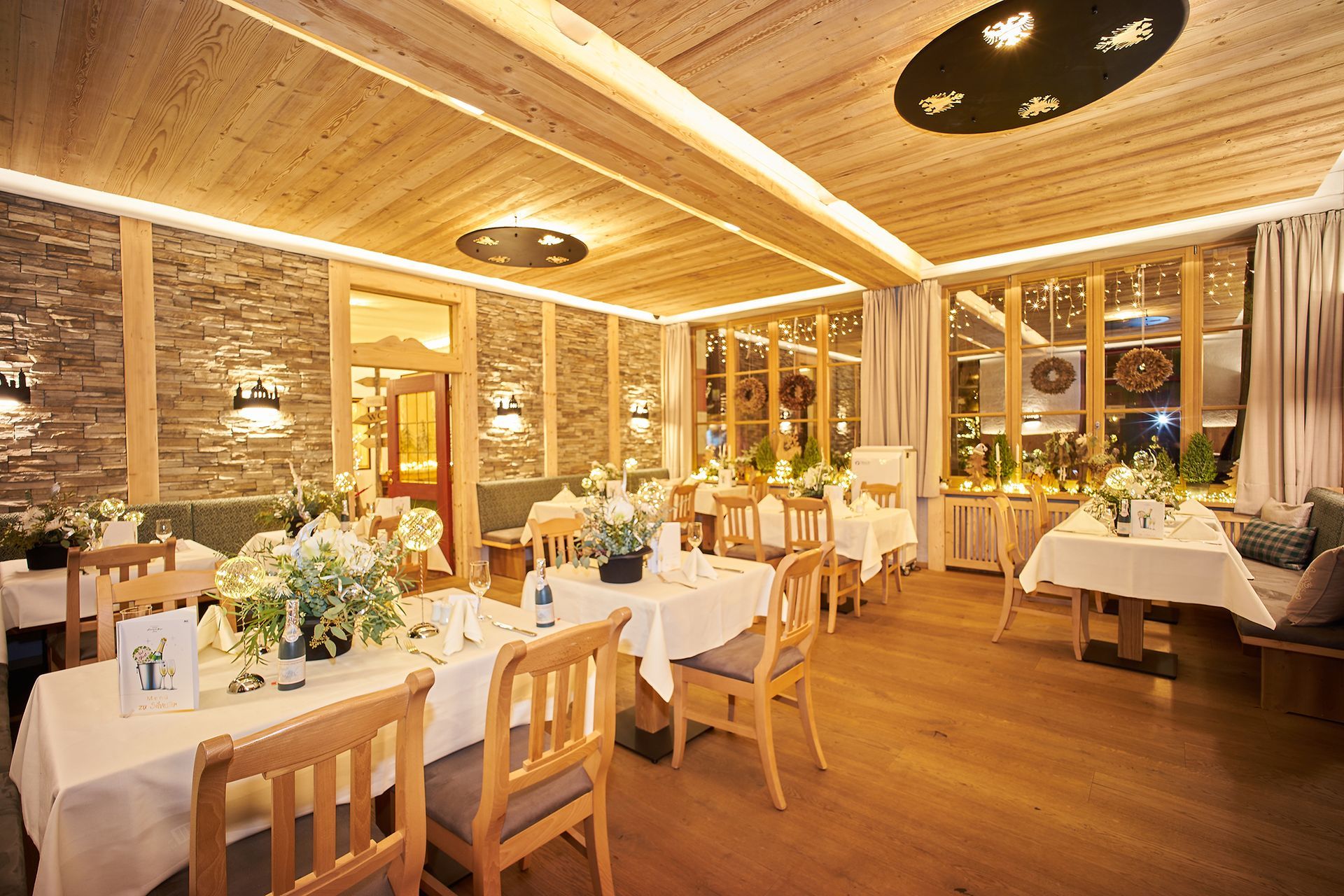 Gemütlicher Gastraum mit Deckenbeleuchtung, Holzdekor und liebevoll eingedeckten Tischen.