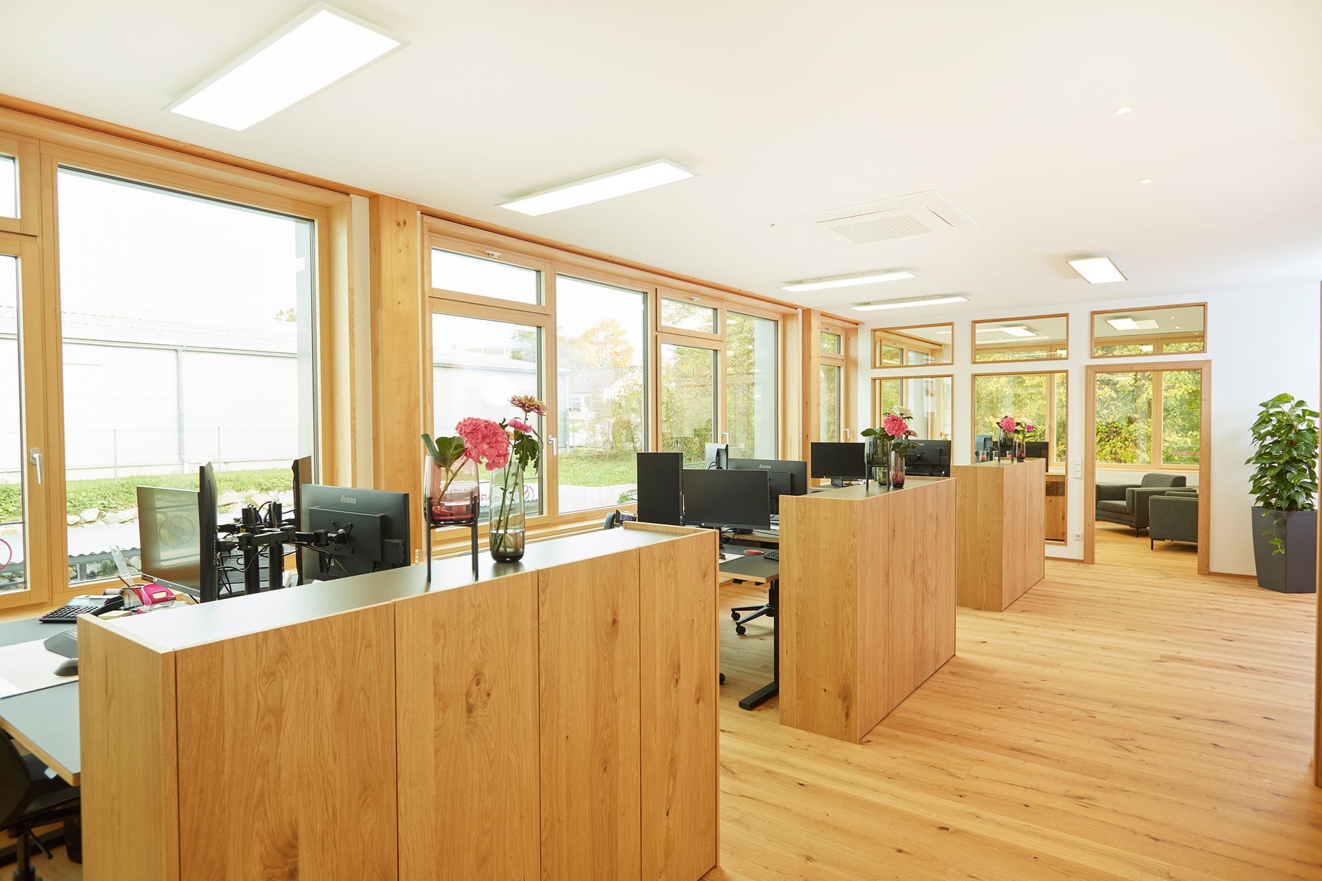 Offene Bürofläche mit Holztrennwänden, Schreibtischen und großen Fensterfronten.