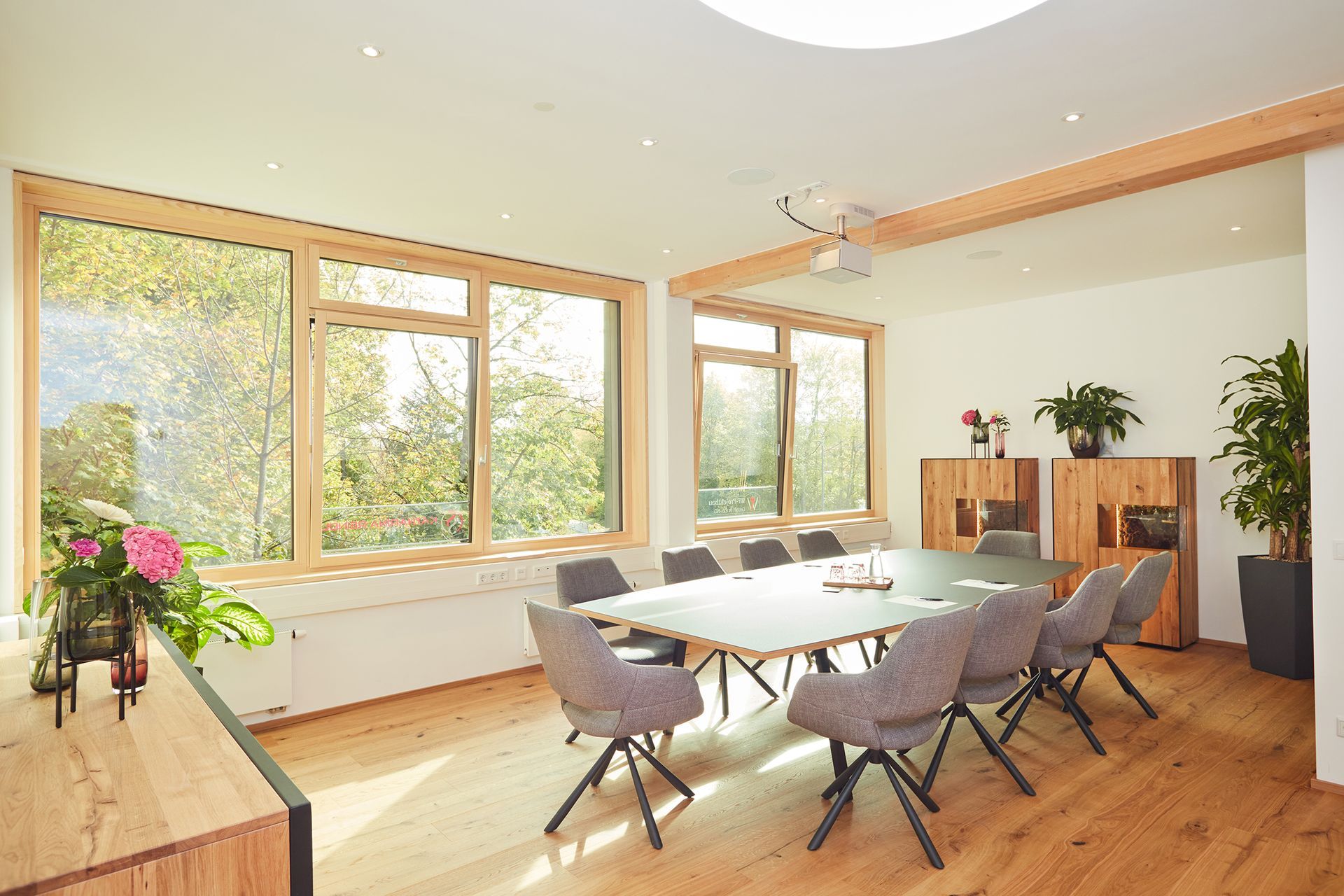 Heller moderner Raum mit großen Fenstern, Holzboden und stilvollen Sitzmöbeln.