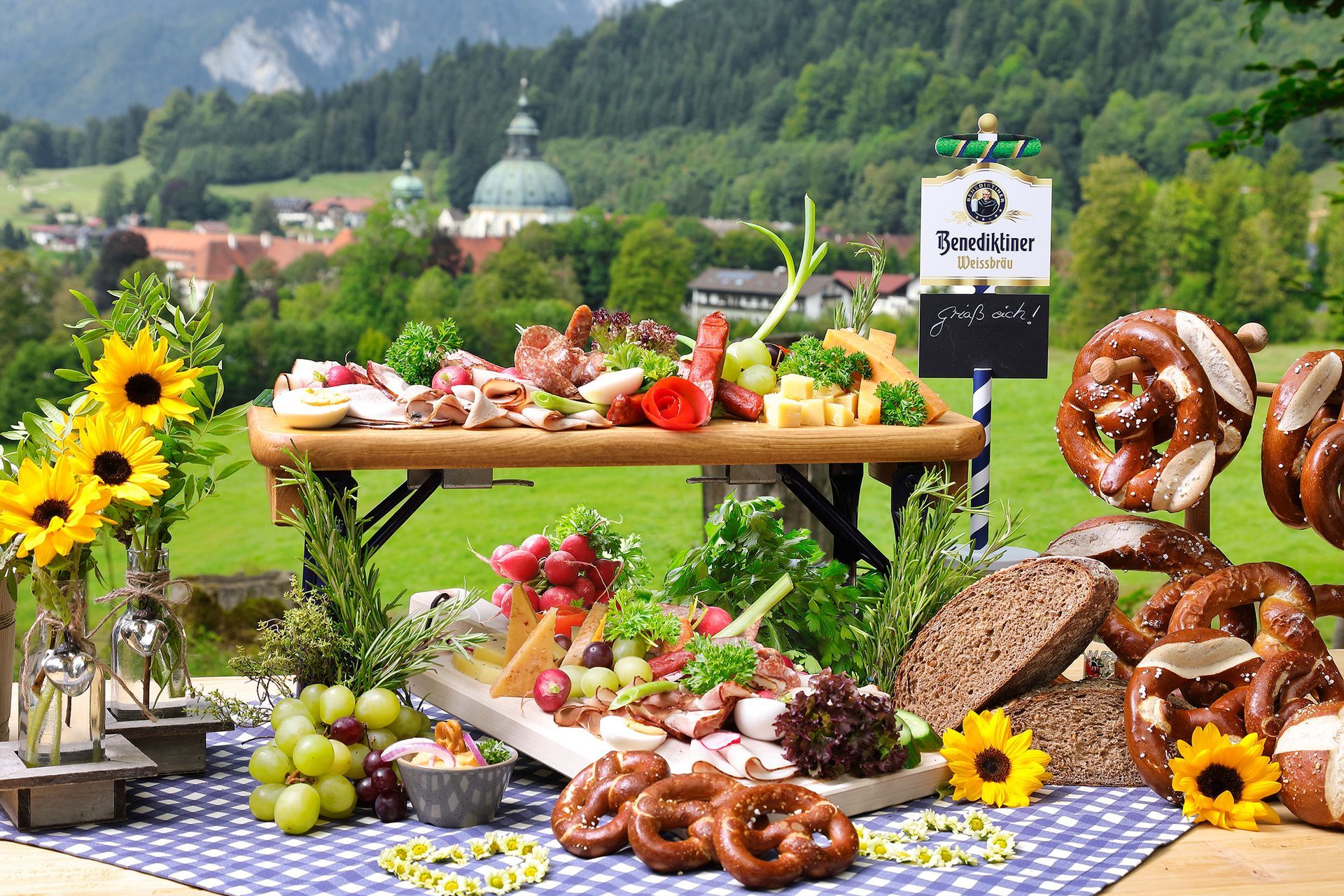 Reich gedeckter bayerischer Brotzeit-Tisch im Freien mit Bergen im Hintergrund.