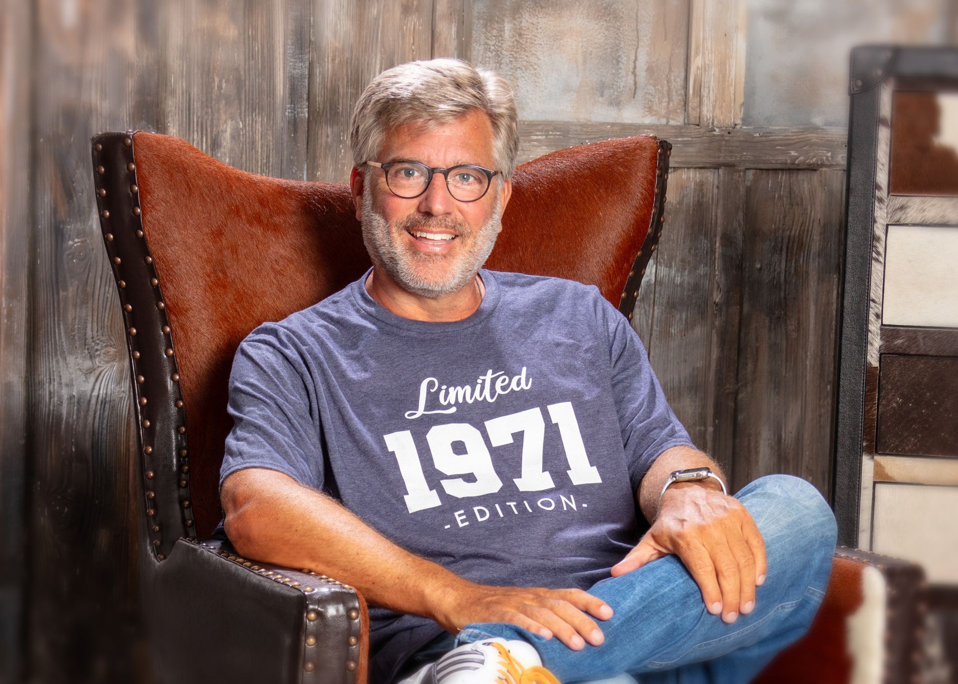 Ein Mann sitzt entspannt in einem Sessel und lächelt in einem gemütlichen, holzvertäfelten Raum.